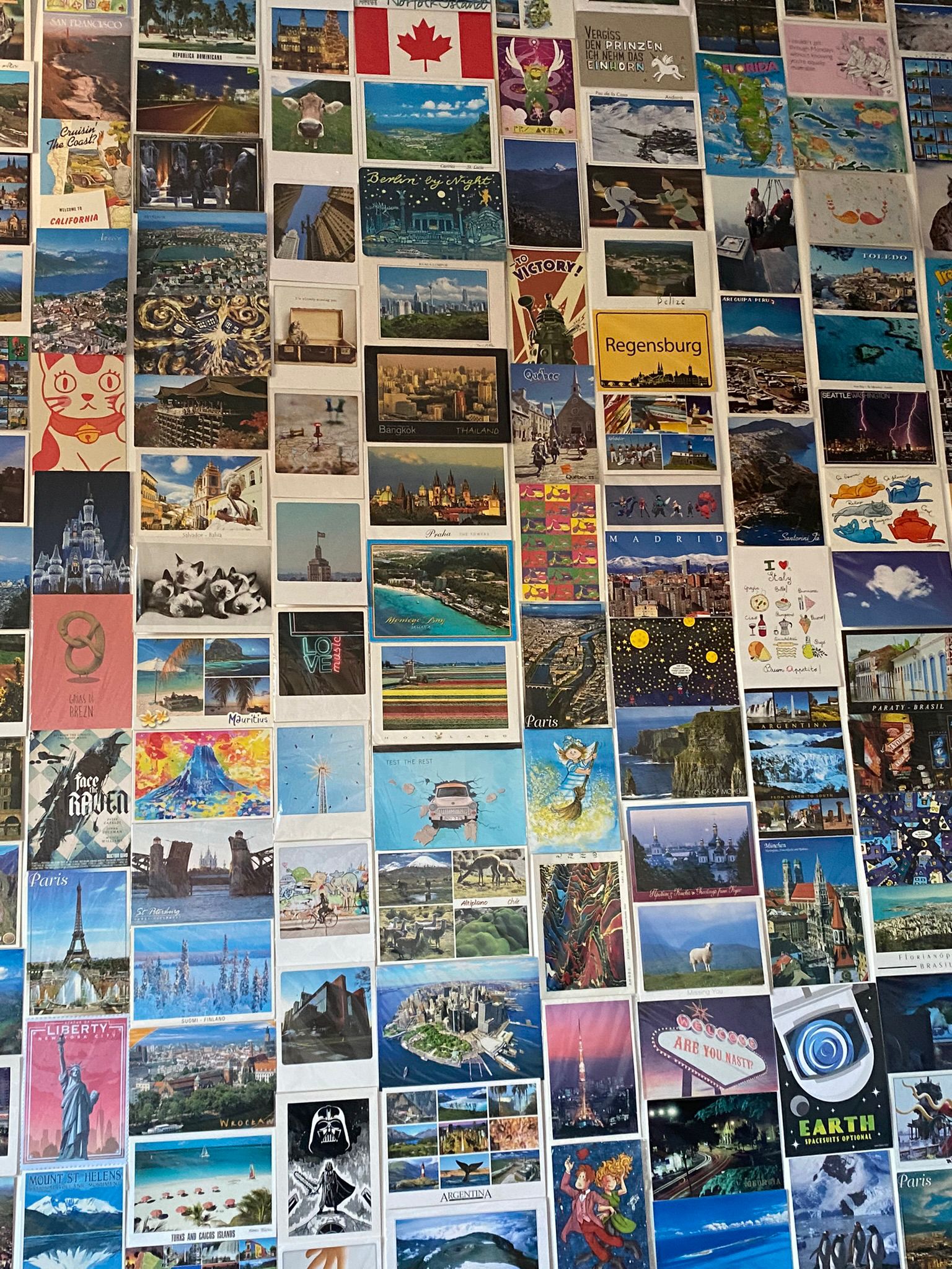 Uma parede com vários cartões postais de papel colados. Eles são coloridos.